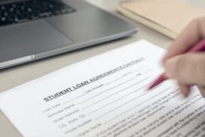 Hand filling a Student Loan form on desk