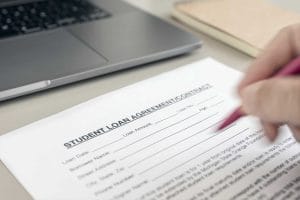 Hand filling a Student Loan form on desk