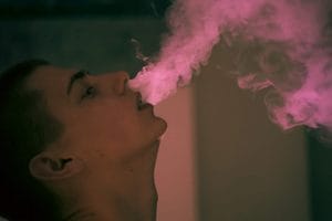 teen boy smokes vape exhales big puffs of smoke